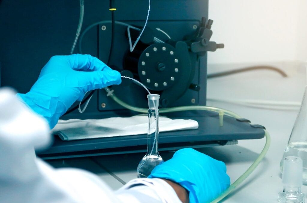 Research scientist hand with blue chemical protective gloves using volumetric flask for doing experiment to determine the levels of heavy metals in solutions by ICP (Inductively Coupled Plasma spectro