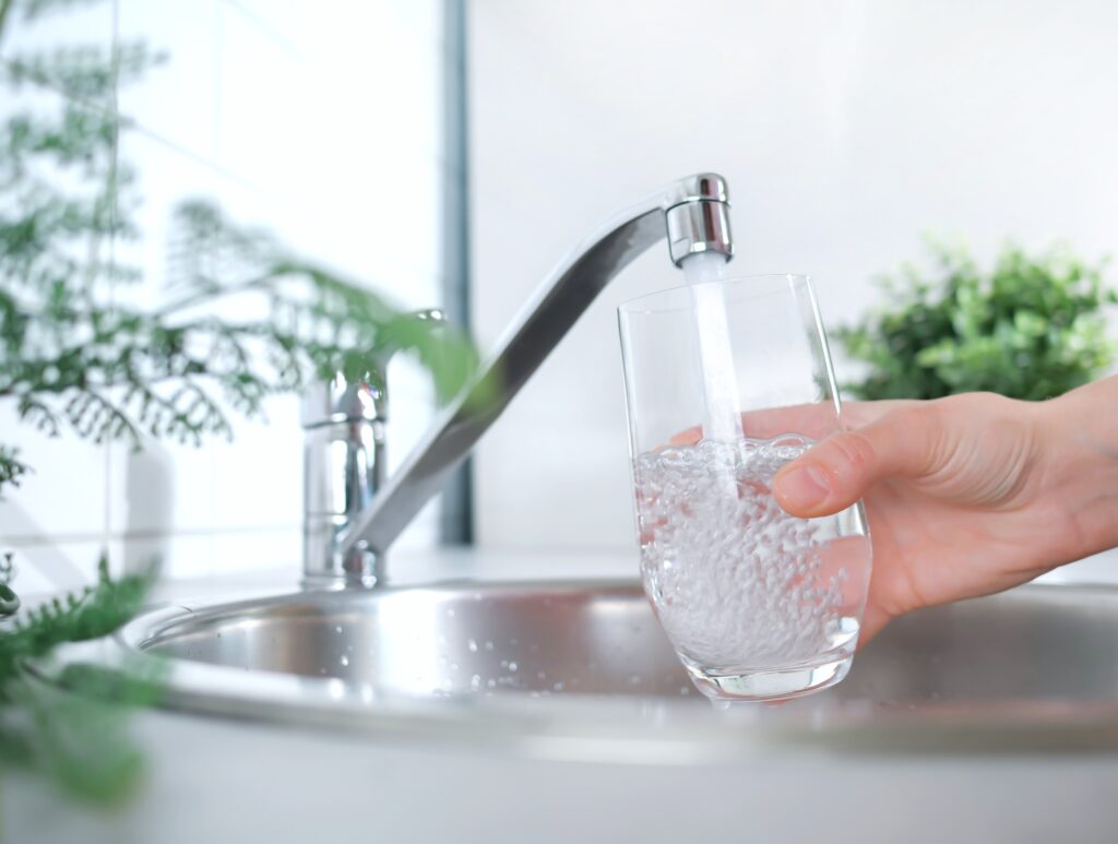 Ein Strahl sauberen Trinkwassers fließt in das Glas. Eine Frau hält ein Glas unter das fließende Wasser aus dem Wasserhahn in der Küche.