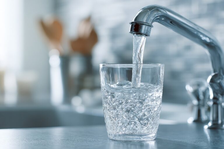 Ein Glas, das an einem Wasserhahn in der Küche mit sauberem Wasser gefüllt wird.